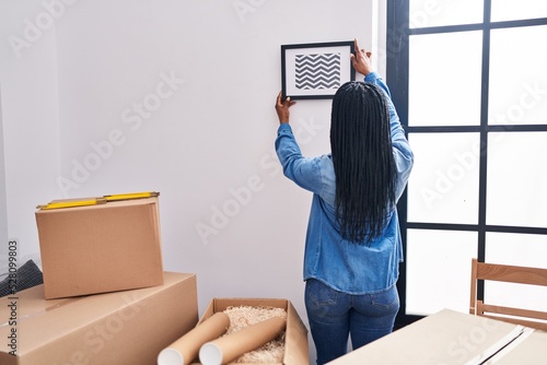African american woman hanging photo on wall at new home