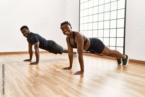 Young african american sporty couple smiling happy doing push-ups exercise at sport center.