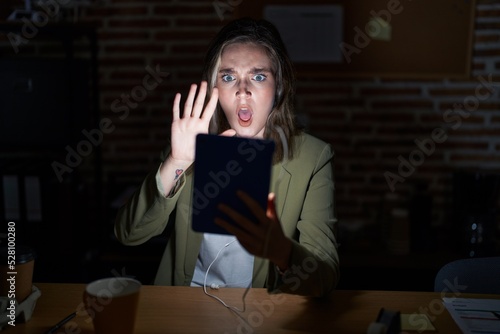 Blonde caucasian woman working at the office at night doing stop gesture with hands palms, angry and frustration expression