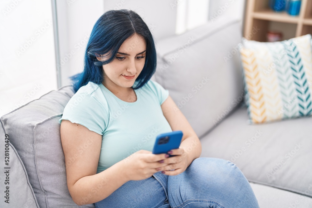 Young caucasian woman using smartphone sitting on sofa at home