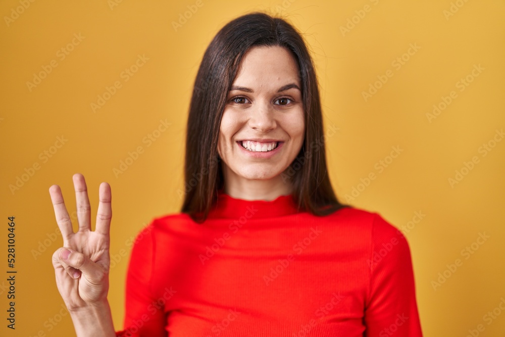 Young hispanic woman standing over yellow background showing and pointing up with fingers number three while smiling confident and happy. Young hispanic woman standing over yellow background showing and pointing up with fingers number three while smiling confident and happy.