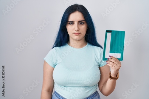 Fotografie Young modern girl with blue hair holding l sign for new driver thinking attitude
