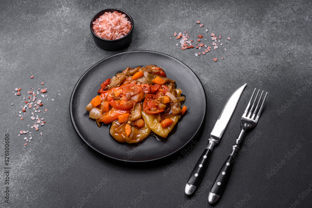 Baked vegetables, eggplant, peppers and carrots on a black plate on concrete background