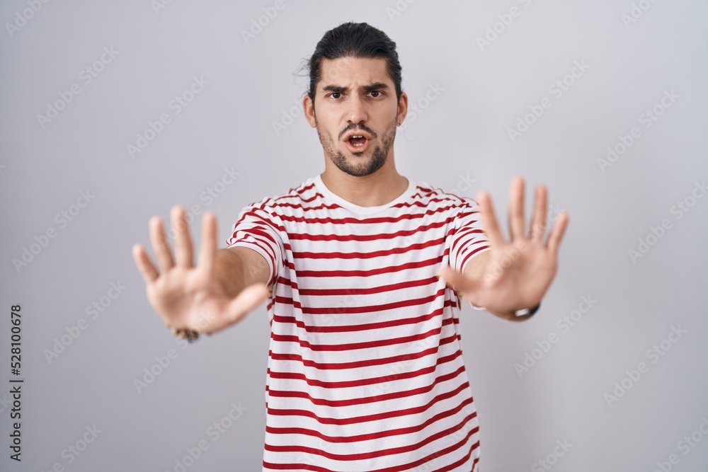 Naklejka premium Hispanic man with long hair standing over isolated background doing stop gesture with hands palms, angry and frustration expression