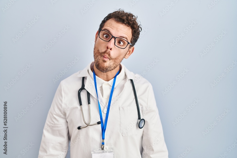 Young hispanic man wearing doctor uniform and stethoscope making fish face with lips, crazy and comical gesture. funny expression. Young hispanic man wearing doctor uniform and stethoscope making fish face with lips, crazy and comical gesture. funny expression.
