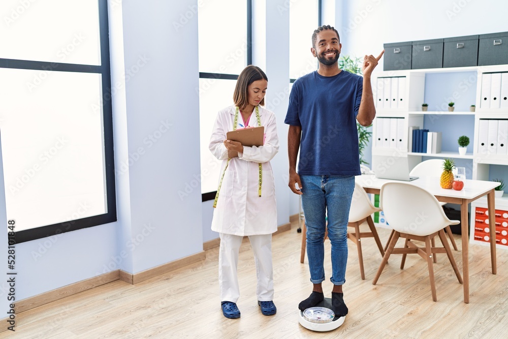 Fototapeta premium Dietitian at the clinic with client checking weight smiling happy pointing with hand and finger to the side