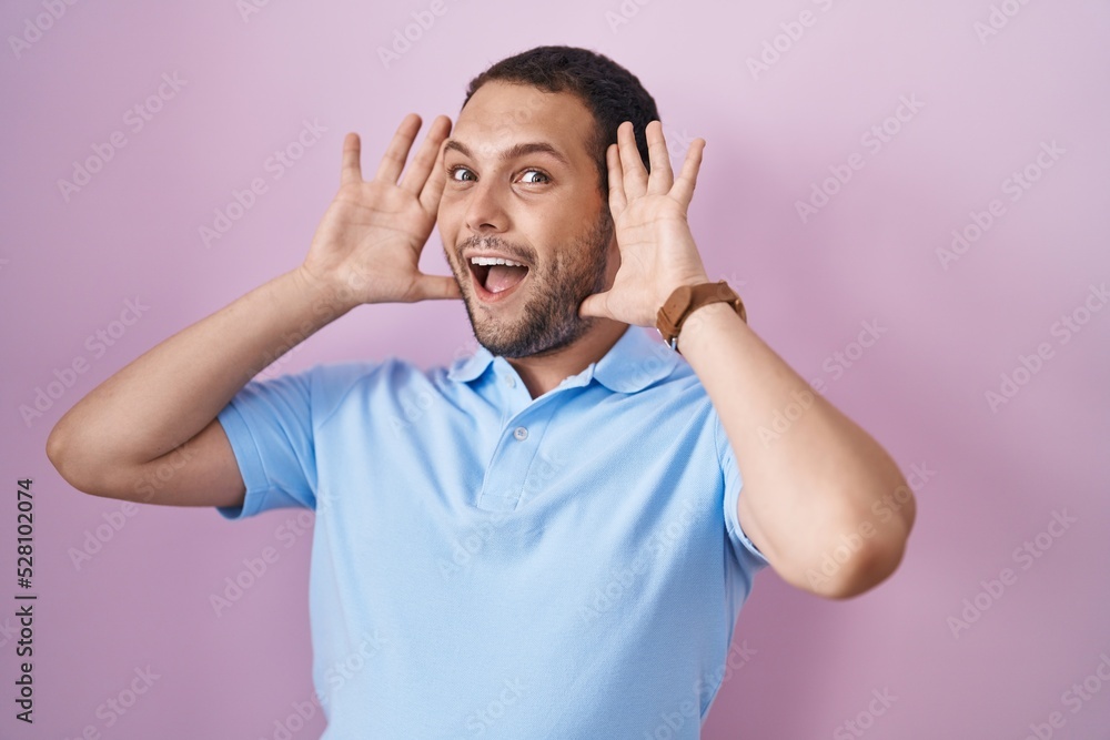Hispanic man standing over pink background smiling cheerful playing peek a boo with hands showing face. surprised and exited Hispanic man standing over pink background smiling cheerful playing peek a boo with hands showing face. surprised and exited