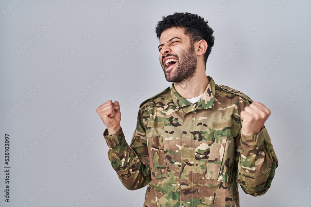 Arab man wearing camouflage army uniform celebrating surprised and amazed for success with arms raised and eyes closed. winner concept.