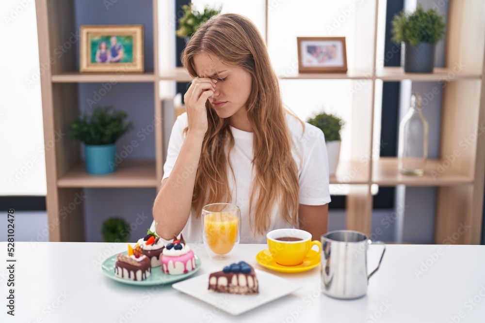 Young caucasian woman eating pastries t for breakfast tired rubbing nose and eyes feeling fatigue and headache. stress and frustration concept.