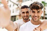Two hispanic men couple hugging each other make selfie by the camera standing at home