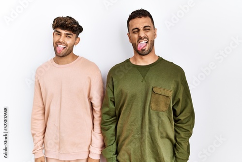 Young gay couple standing over isolated white background sticking tongue out happy with funny expression. emotion concept.