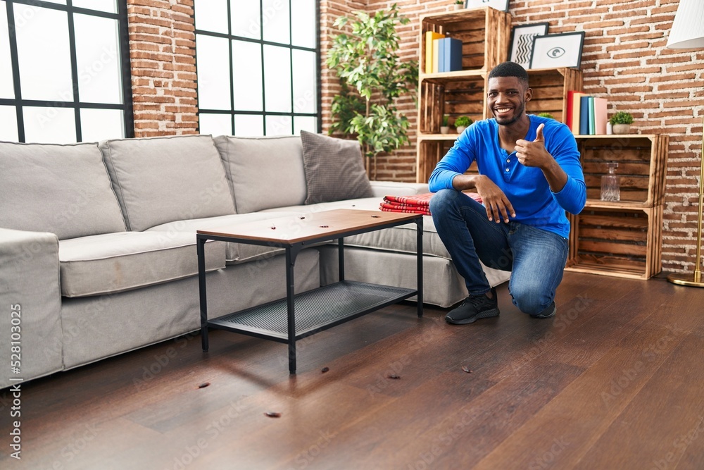 Obraz premium African american man at home with cockroach infestation smiling happy and positive, thumb up doing excellent and approval sign