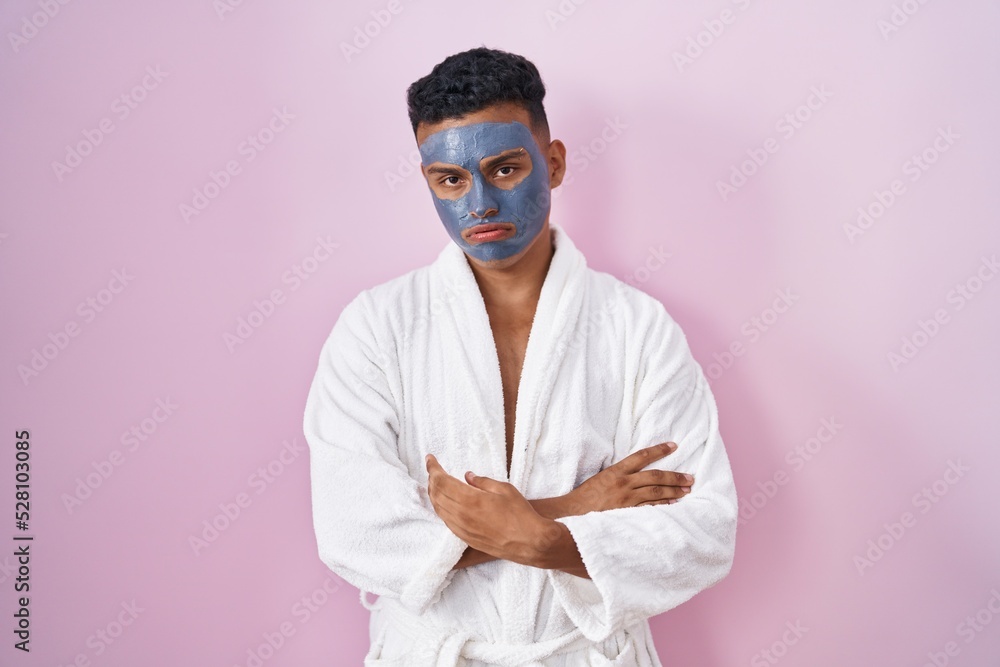 Young hispanic man wearing beauty face mask and bath robe looking sleepy and tired, exhausted for fatigue and hangover, lazy eyes in the morning. Young hispanic man wearing beauty face mask and bath robe looking sleepy and tired, exhausted for fatigue and hangover, lazy eyes in the morning.