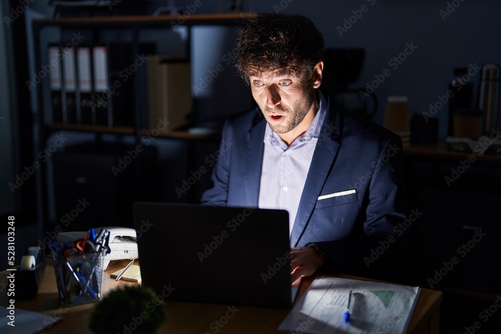 Hispanic young man working at the office at night afraid and shocked with surprise expression, fear and excited face. Hispanic young man working at the office at night afraid and shocked with surprise expression, fear and excited face.