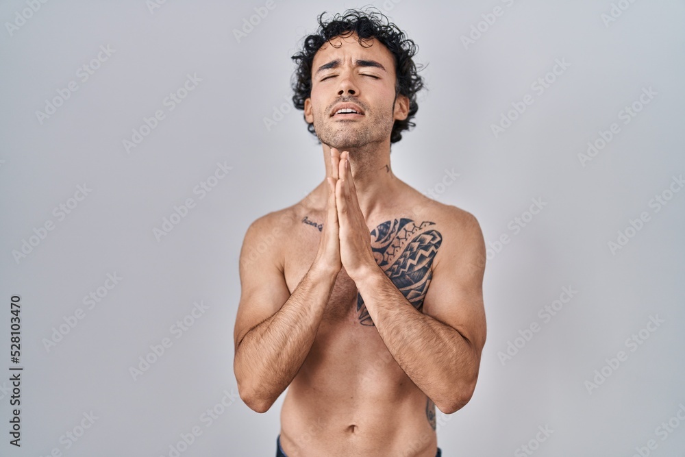 Fototapeta premium Hispanic man standing shirtless begging and praying with hands together with hope expression on face very emotional and worried. begging.