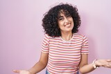 Young middle east woman standing over pink background smiling cheerful with open arms as friendly welcome, positive and confident greetings