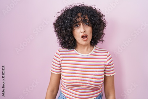 Young middle east woman standing over pink background in shock face, looking skeptical and sarcastic, surprised with open mouth © Krakenimages.com