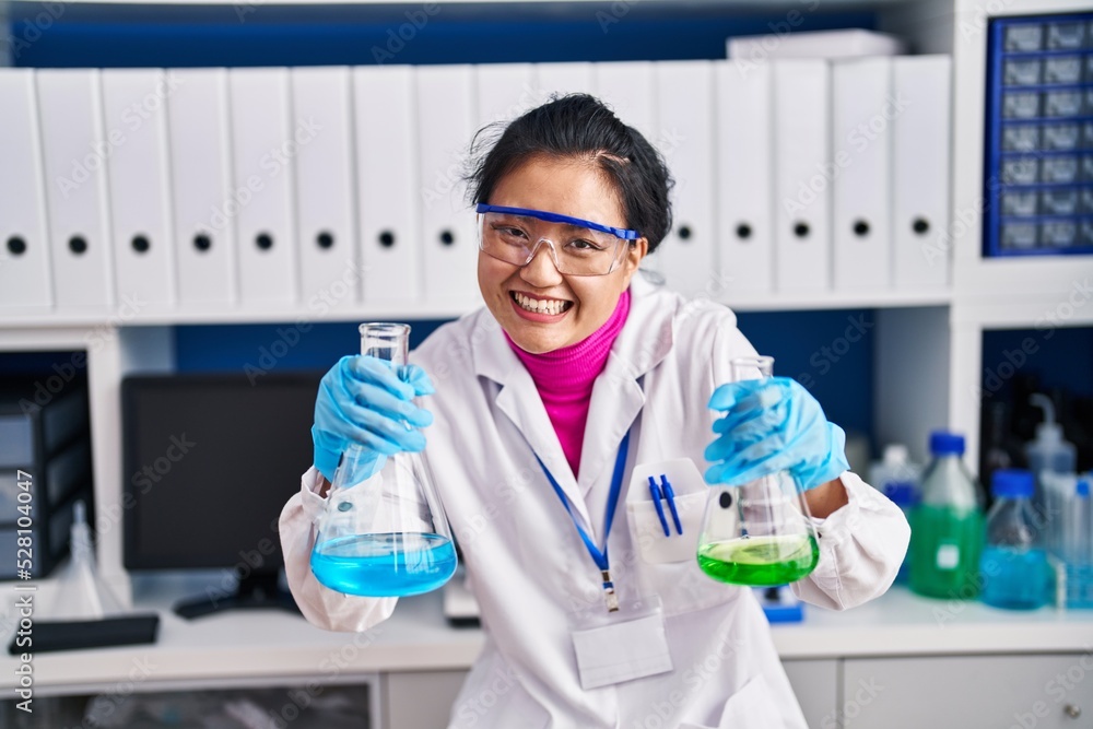 Young asian woman working at scientist laboratory smiling and laughing hard out loud because funny crazy joke.