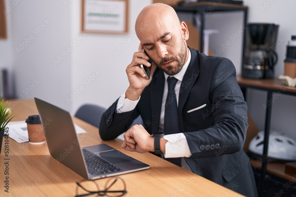 Young bald man business worker talking on smartphone looking watch at office Young bald man business worker talking on smartphone looking watch at office