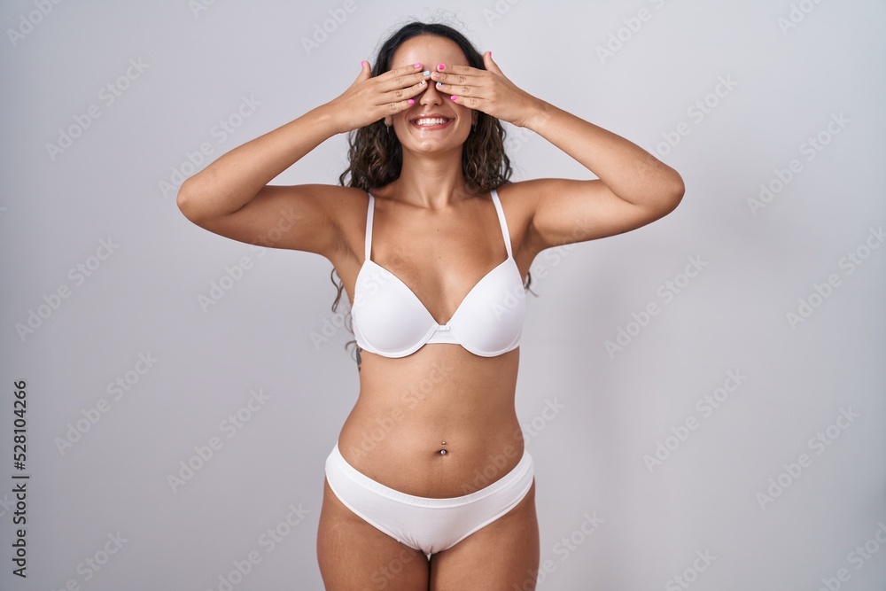 Young hispanic woman wearing white lingerie covering eyes with hands smiling cheerful and funny. blind concept. Young hispanic woman wearing white lingerie covering eyes with hands smiling cheerful and funny. blind concept.