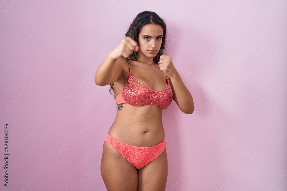 Obraz premium Young hispanic woman wearing lingerie over pink background punching fist to fight, aggressive and angry attack, threat and violence