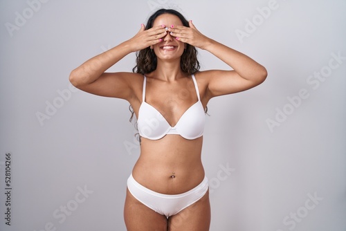 Young hispanic woman wearing white lingerie covering eyes with hands smiling cheerful and funny. blind concept. © Krakenimages.com