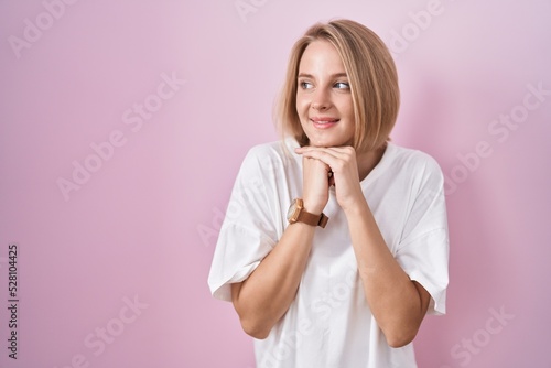 Young caucasian woman standing over pink background laughing nervous and excited with hands on chin looking to the side