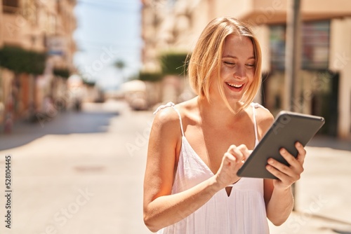 Young blonde woman smiling confident using touchpad at street