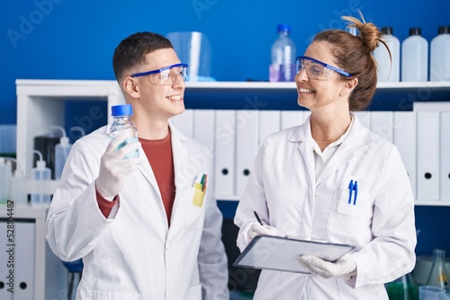 Man and woman scientists write on document holding bottle at laboratory