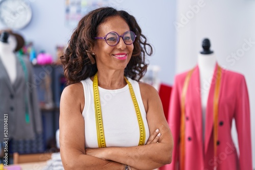 Middle age woman tailor smiling confident standing with arms crossed gesture at clothing factory