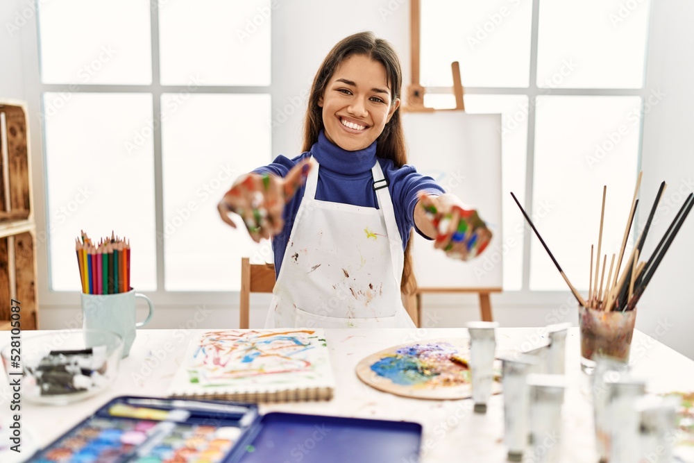 Young brunette woman at art studio with painted hands approving doing positive gesture with hand, thumbs up smiling and happy for success. winner gesture. Young brunette woman at art studio with painted hands approving doing positive gesture with hand, thumbs up smiling and happy for success. winner gesture.