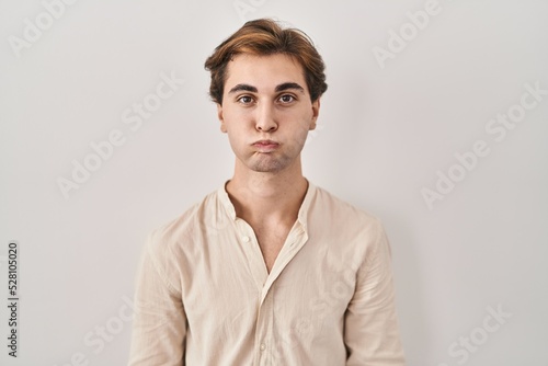 Young man standing over isolated background puffing cheeks with funny face. mouth inflated with air, crazy expression.