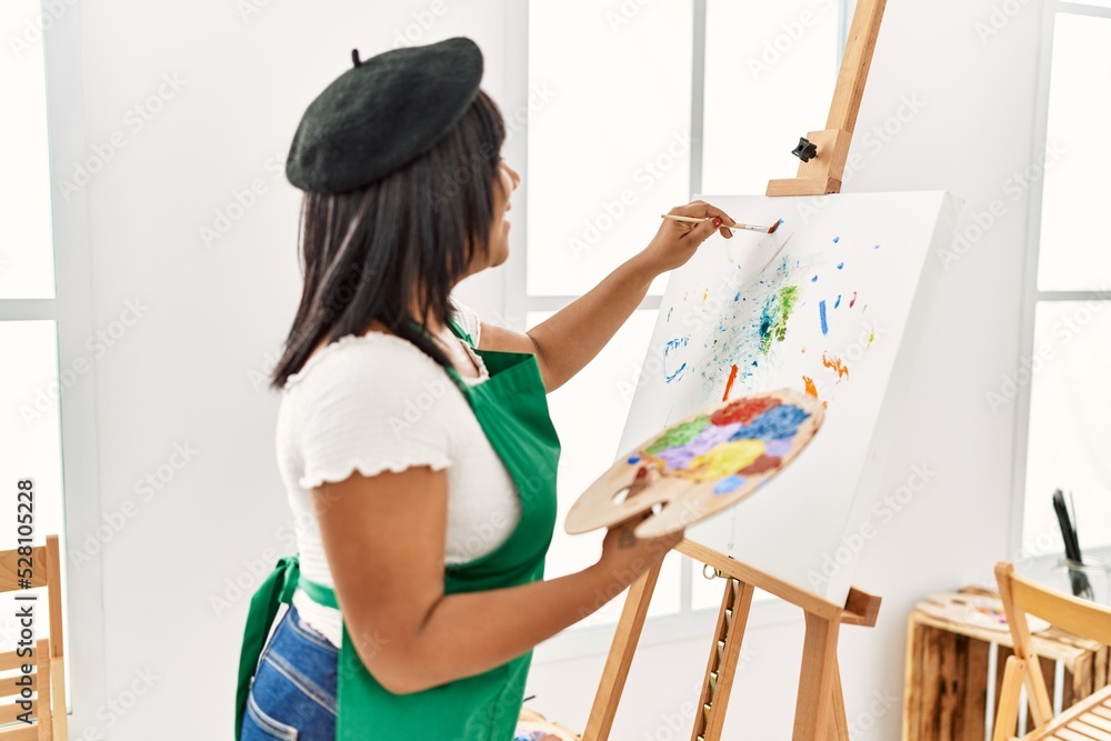 Hispanic brunette woman painting on canvas at art studio