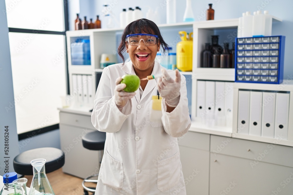 Hispanic woman working at scientist laboratory with apple celebrating crazy and amazed for success with open eyes screaming excited. Hispanic woman working at scientist laboratory with apple celebrating crazy and amazed for success with open eyes screaming excited.