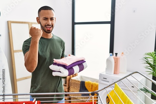 African american man holding folded laundry from clothline annoyed and frustrated shouting with anger, yelling crazy with anger and hand raised photo