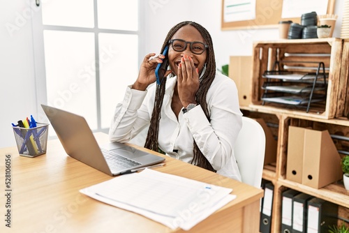 Vászonkép Black woman with braids working at the office speaking on the phone laughing and