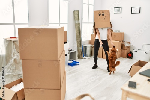 Photography Young hispanic woman wearing funny cardboard on head playing with dogs at new ho