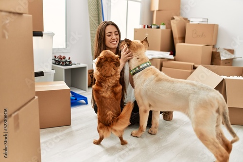 Sticker Young hispanic woman smiling confident sitting on floor with dogs at new home