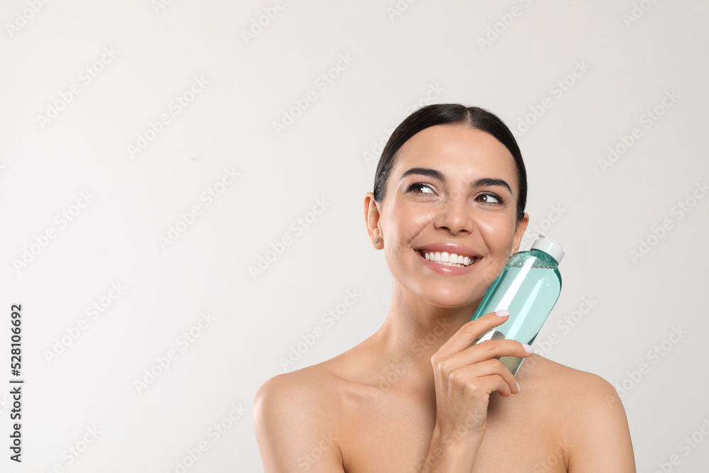 Young woman with micellar water on light grey background, space for text Young woman with micellar water on light grey background, space for text