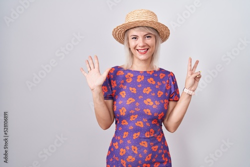 Young caucasian woman wearing flowers dress and summer hat showing and pointing up with fingers number seven while smiling confident and happy.