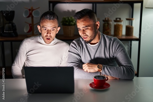 Homosexual couple using computer laptop in shock face, looking skeptical and sarcastic, surprised with open mouth