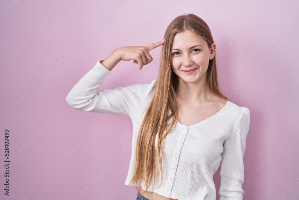 Young caucasian woman standing over pink background smiling pointing to head with one finger, great idea or thought, good memory Young caucasian woman standing over pink background smiling pointing to head with one finger, great idea or thought, good memory
