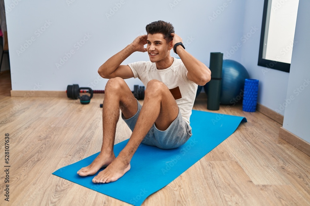 Obraz premium Young hispanic man smiling confident training abs exercise at sport center