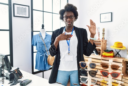 African young woman working as manager at retail boutique swearing with hand on chest and open palm, making a loyalty promise oath