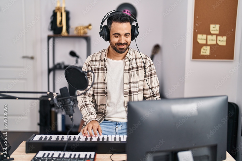 Young hispanic man musician singing song playing piano keyboard at music studio