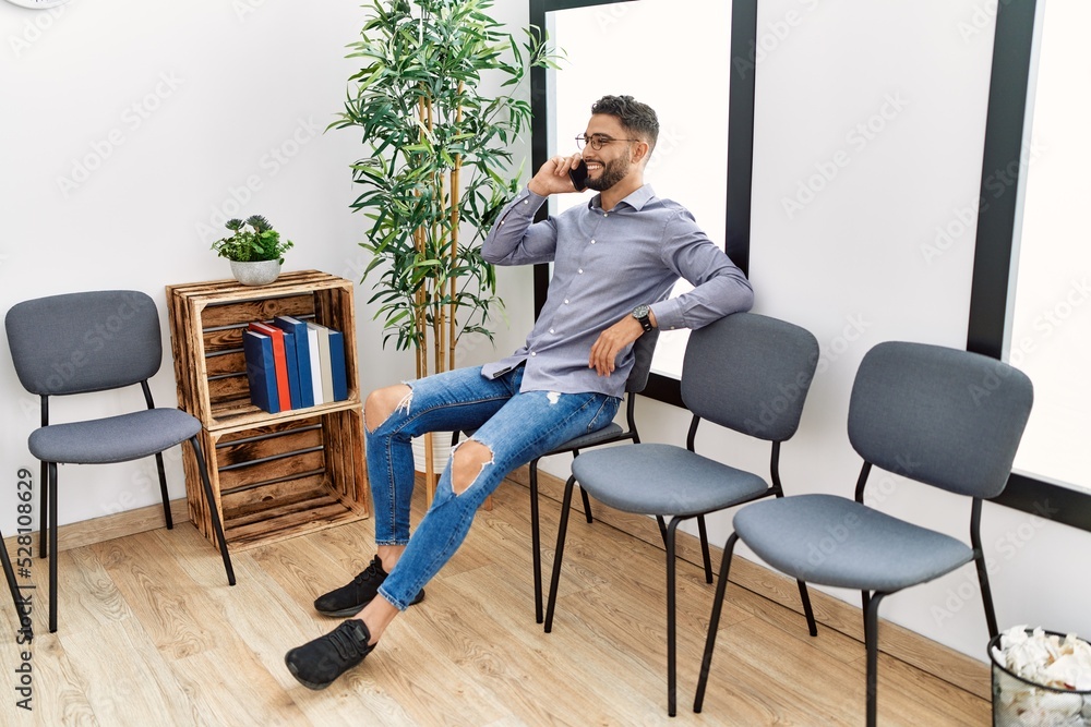 Young arab man talking on the smartphone sitting on chair at waiting room