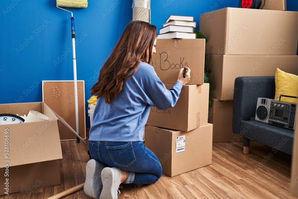 Fototapeta premium Young hispanic woman on back view writing on books package at new home