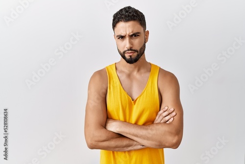 Young handsome man with beard standing over isolated background skeptic and nervous, disapproving expression on face with crossed arms. negative person.