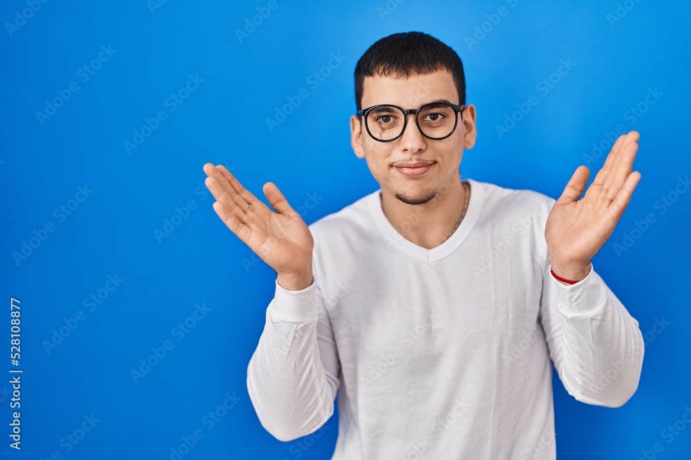 Young arab man wearing casual white shirt and glasses clueless and confused expression with arms and hands raised. doubt concept. Young arab man wearing casual white shirt and glasses clueless and confused expression with arms and hands raised. doubt concept.