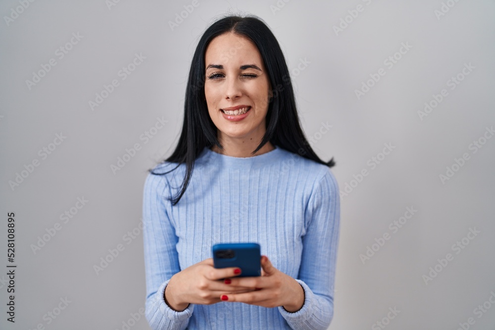 Hispanic woman using smartphone winking looking at the camera with sexy expression, cheerful and happy face. Hispanic woman using smartphone winking looking at the camera with sexy expression, cheerful and happy face.